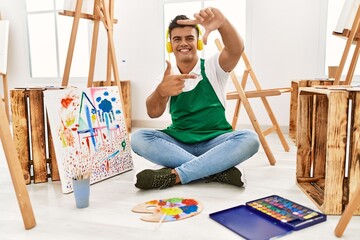 Sticker - Young hispanic man at art studio smiling making frame with hands and fingers with happy face. creativity and photography concept.