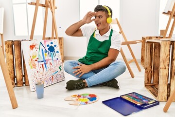 Poster - Young hispanic man at art studio very happy and smiling looking far away with hand over head. searching concept.