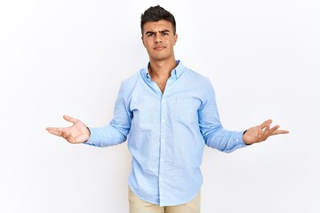 Poster - Young hispanic man wearing business shirt standing over isolated background clueless and confused with open arms, no idea concept.