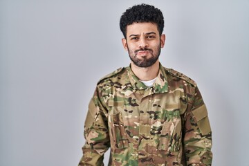 Canvas Print - Arab man wearing camouflage army uniform puffing cheeks with funny face. mouth inflated with air, crazy expression.