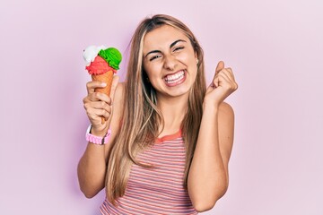 Canvas Print - Beautiful hispanic woman holding ice cream screaming proud, celebrating victory and success very excited with raised arm