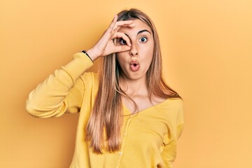 Canvas Print - Beautiful hispanic woman wearing casual yellow sweater doing ok gesture shocked with surprised face, eye looking through fingers. unbelieving expression.