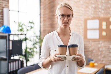 Canvas Print - Young caucasian woman working at the office holding coffee cups clueless and confused expression. doubt concept.