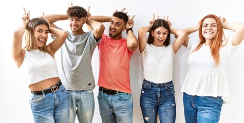 Sticker - Group of young friends standing together over isolated background posing funny and crazy with fingers on head as bunny ears, smiling cheerful