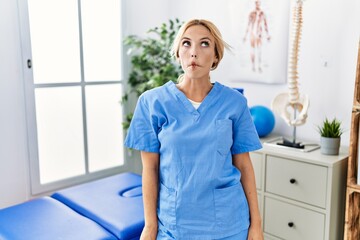 Poster - Beautiful blonde physiotherapist woman working at pain recovery clinic making fish face with lips, crazy and comical gesture. funny expression.