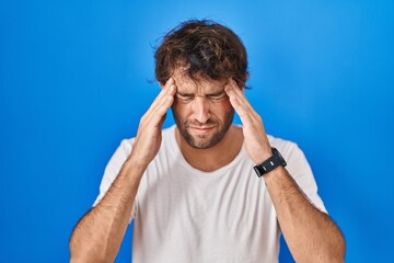 Poster - Hispanic young man standing over blue background with hand on head, headache because stress. suffering migraine.