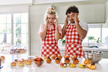 Canvas Print - Couple of wife and husband cooking pastries at the kitchen with hand on head for pain in head because stress. suffering migraine.