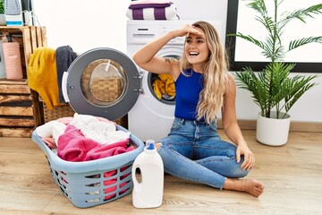 Sticker - Young beautiful woman doing laundry sitting by wicker basket very happy and smiling looking far away with hand over head. searching concept.