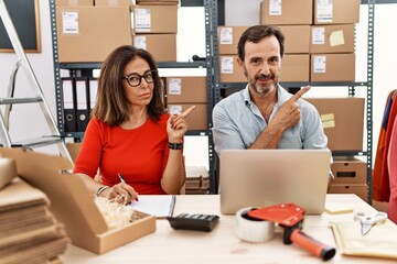 Sticker - Middle age couple working at small business ecommerce pointing with hand finger to the side showing advertisement, serious and calm face