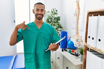 Poster - African american physiotherapist man working at pain recovery clinic looking confident with smile on face, pointing oneself with fingers proud and happy.