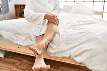 Middle Age Grey-haired Woman Massaging Legs With Cream Sitting On Bed At Bedroom