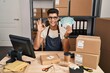© Krakenimages.com - Young hispanic man working at small business ecommerce holding brazilian reals doing ok sign with fingers, smiling friendly gesturing excellent symbol