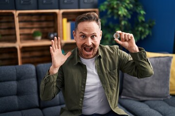 Sticker - Middle age caucasian man holding virtual currency bitcoin celebrating victory with happy smile and winner expression with raised hands