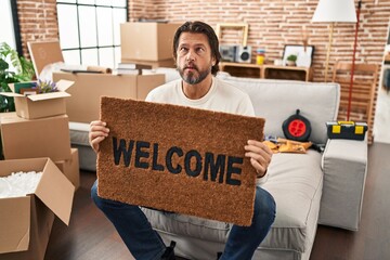 Sticker - Handsome middle age man holding welcome doormat at new home making fish face with mouth and squinting eyes, crazy and comical.