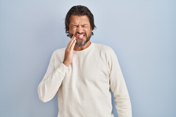 Poster - Handsome middle age man wearing casual sweater over blue background touching mouth with hand with painful expression because of toothache or dental illness on teeth. dentist