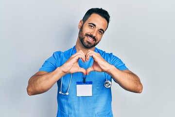 Sticker - Handsome hispanic man with beard wearing doctor uniform smiling in love showing heart symbol and shape with hands. romantic concept.