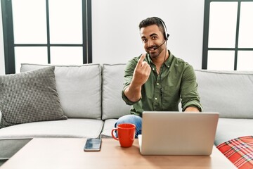 Poster - Young hispanic man with beard wearing call center agent headset working from home beckoning come here gesture with hand inviting welcoming happy and smiling