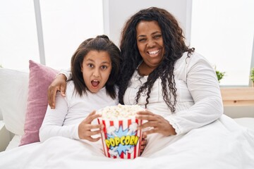 Poster - Mother and young daughter eating popcorn in the bed celebrating crazy and amazed for success with open eyes screaming excited.