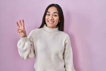 Poster - Young south asian woman standing over pink background showing and pointing up with fingers number three while smiling confident and happy.