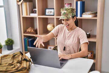 Young south asian woman wearing camouflage army uniform doing video call celebrating achievement with happy smile and winner expression with raised hand