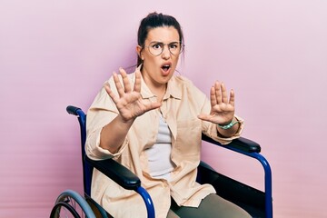 Sticker - Young hispanic woman sitting on wheelchair doing stop gesture with hands palms, angry and frustration expression