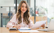 © Phushutter - Pretty Asian woman sitting in the office, calculator, working on data, charts and documents on the table in business workspace. Looking camera.