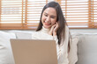 © KMPZZZ - Happy cheerful, satisfied asian young freelancer woman, girl sitting on sofa or couch, using laptop computer in living room at home, looking and smiling at screen, entrepreneur enjoying with work, wfh