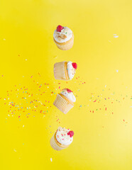 Light berry dessert - cupcakes with air cream and fresh raspberries in a frozen flight on a yellow background with shiny confetti. Sweet food, treat for the holiday. Restaurant, hotel, bakery.