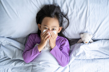 Top view Asian child girl sick with sneezing on the nose and cold cough on tissue paper because weak, Sick child with fever and illness in bed.