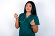 © Roquillo - Doctor hispanic woman wearing surgeon uniform over white wall doing money gesture with hands, asking for salary payment, millionaire business