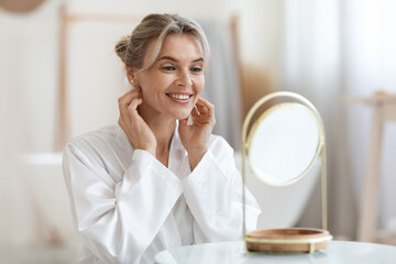 Cheerful beautiful adult lady using hydrating face cream