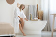 Beautiful blonde lady filling bath with water