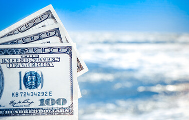 Girl holding money bill of 300 dollars on background of sea ocean waves and blue sky close-up. Hand wave sea ocean money dollars vacation. Concept finance money holiday traveling