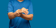 © meeboonstudio - Close-up of hand female suffering from wrist pain while standing on a blue background