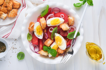 Tuscan Panzanella salad. Fresh tomatoes salad with basil leaves, eggs, olive oil and onion in white bowl on light background. Vegetarian panzanella salad. Mediterranean healthy food. Top view.