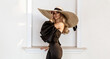 © marcink3333 - Spring, summer fashion. High fashion model. Glamour, stylish elegant woman in black jumpsuit and big hat. Female model in stylish look in the city. Travel model. Outdoor shoot. Vogue. Elegance.