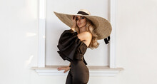 Spring, Summer Fashion. High Fashion Model. Glamour, Stylish Elegant Woman In Black Jumpsuit And Big Hat. Female Model In Stylish Look In The City. Travel Model. Outdoor Shoot. Vogue. Elegance.