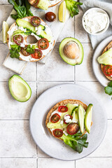 Wall Mural - Bagels sandwich topped with cream cheese, farm cottage cheese, avocado, tomatoes, cucumbers and salad leaves, tilled background. Healthy breakfast food.