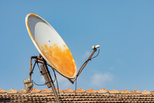 Old Rusty Satellite Dish Antenna On A Tiled Roof Against Blue Sky