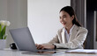 © wichayada - Happy young asian businesswoman sitting on her workplace in the office. Young woman working at laptop in the office.