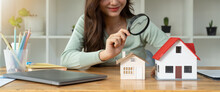 Looking For Real Estate Agency, Property Insurance, Mortgage Loan Or New House. Woman With Magnifying Glass Over A Wooden House At Her Office