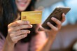 © Benixs - Close-up or closeup of young woman's hand is holding gold credit card and using smartphone with happiness feeling. Female shopper flip her credit card to make purchase online transactions.