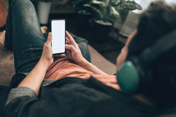 Men hand holding texting  mobile phone with blank screen and wearing headphone on sofa at home. Relax home concept.