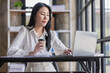 © David - Portrait of Attractive Asian woman working with laptop computer in the office hand holding cup of coffee.