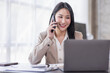 © David - Asian businesswoman working at home with a laptop and talking on smartphone
