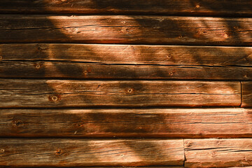 The wall of village house in close up. Old wooden wall cracked by time. Minimalistic brown horizontal wooden background with shadows from trees.