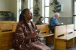 © pressmaster - Young Christian black woman in casual dress kkeeping her eyes closed while sitting on bench in church and saying prayers to Lord