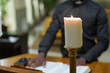 White burning candle on background of priest reading verses from Holy Bible while standing by pulpit and telling sermon during church service