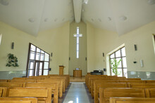 Empty Hall For Church Services With Aisle Between Two Rows Of Wooden Benches For Parishioners And Cross Above Pulpit Of Pastor