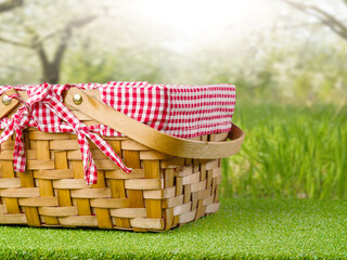 Wall Mural - A straw picnic basket on a green lawn against the backdrop of a wonderful summer nature. The concept is a picnic in nature, recreation, fun, environmental protection.